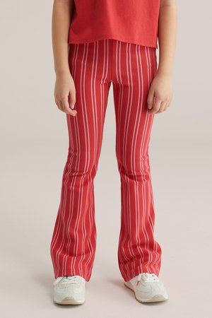 Barn iført røde og hvide lodrette stribede vide bukser, rød skjorte og hvide sneakers, stående på en neutral baggrund.