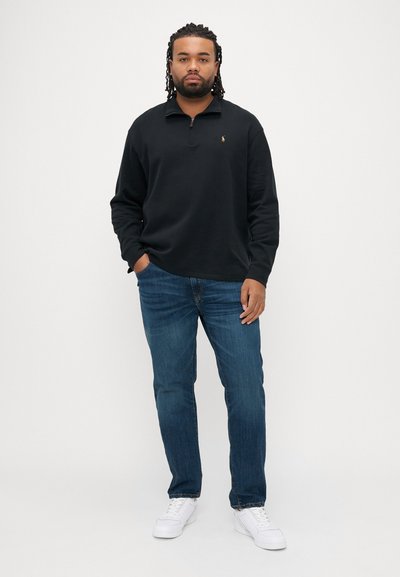 Μαύρο φούτερ με φερμουάρ, μπλε τζιν και λευκά αθλητικά παπούτσια. Το φούτερ έχει ένα μικρό λογότυπο στο αριστερό στήθος. Casual εφαρμογή και στυλ.