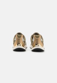 Bronse- og olivenfargede joggesko med teksturert finish, hvite detaljer og en gull logo på hælen. Har polstret krage og hvit såle.