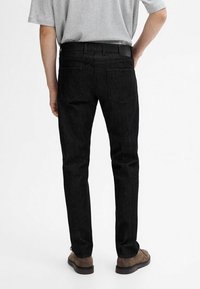 Jeans in denim nero con una vestibilità slim, con due tasche posteriori e una consistenza liscia. Indossati con una maglietta grigia e calzature marroni.