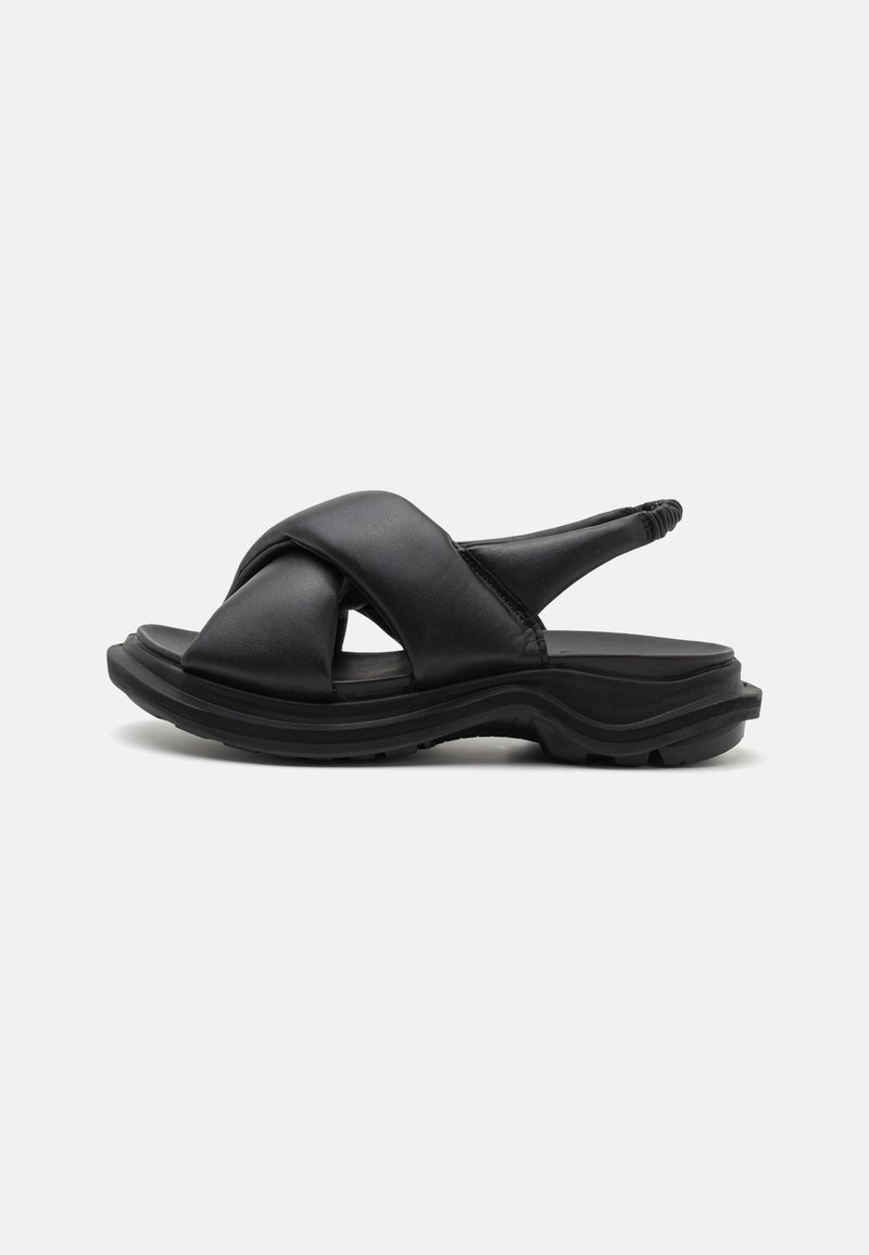 Sandale en cuir noir avec brides croisées matelassées, bride arrière élastique, semelle épaisse texturée et design ouvert à l'avant et au talon.