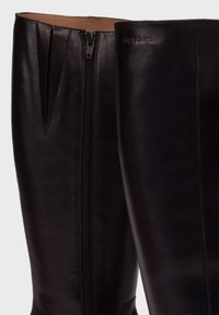 Bottes noires en cuir montantes au genou avec fermeture éclair sur le côté, texture lisse et logo discret sur la partie supérieure.