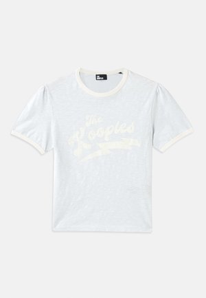 T-shirt bleu clair à manches courtes avec un col crème et des manches bouffantes, arborant le texte blanc "The Kooples" avec un design d'éclair.