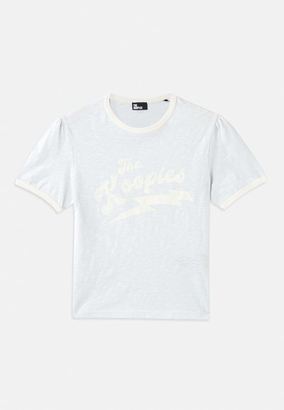 Hele sinise lühikese varrukaga T-särk, millel on kreemjas krae ja puhvvarrukad, ning millel on valge tekst "The Kooples" koos välku kujutava disainiga.