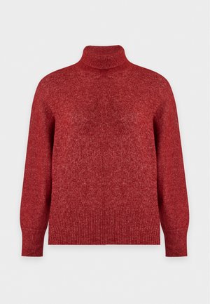 Femme portant un pull à col roulé rouge, une jupe midi en cuir brun foncé avec une fente devant et des bottines noires, debout devant un fond uni.