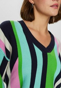 Pulover s V-izrezom, okrašen z navy, metino zeleno, svetlo roza in belo stripom. Narejen iz mehkega pletenega materiala z vidno teksturo.