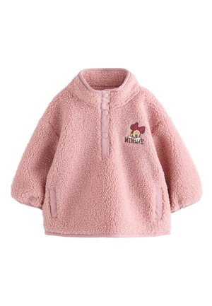 Maluch ubrany w różowy polarowy sweter z haftem Myszki Miki, niebieskie dżinsy i białe trampki, stojący na pomarańczowej okrągłej platformie.