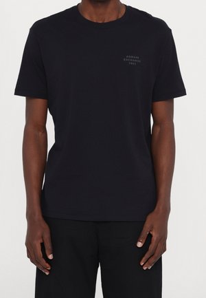 Schwarzes T-Shirt mit kurzen Ärmeln aus Baumwolle. Mit einem dezenten Logodruck auf der Brust. Einfaches Design mit klassischer Passform und Rundhalsausschnitt.