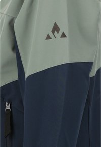 Vandrejakke med en lys grøn overdel og mørk navy underdel, lavet af glat, holdbart materiale med et logo nær skulderen.