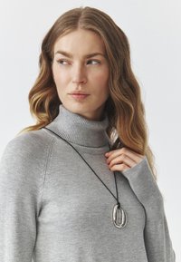Gray turtleneck sweater with ribbed texture; features a black necklace with a polished metallic pendant in an organic, oval shape.