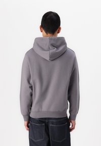 Sudadera gris con un bolsillo frontal tipo canguro, capucha con cordones y puños acanalados, combinada con jeans de mezclilla oscuros de corte relajado.