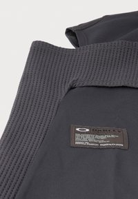 Fekete sportos anyag, texturált bordázott nyakrésszel, valamint varrott címkével, amely márkát és ápolási információkat tartalmaz, és a varrásba van bevarrva.