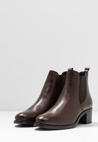 Botas de tobillo de cuero marrón con un acabado suave, paneles laterales elásticos y un tacón bajo y grueso. Diseño de punta redondeada.