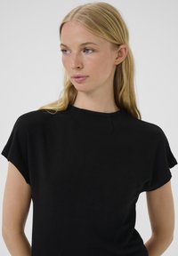 Čierny pletený top s krátkymi rukávmi a okrúhlym výstrihom. Vyrobený z textúrovanej látky s jemnými švami na pleciach.