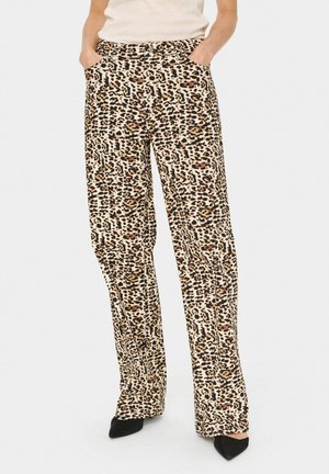 Leopardmönstrade vida byxor i beige och svart, med sidofickor och en mjuk textur, kombinerade med svarta spetsiga skor.