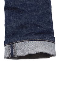 Tummansinisiä farkkuja, joiden lahkeensuissa on harmaa vuori, siisti helma ja näkyviä ompelu yksityiskohtia reunalla.