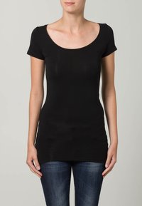 Fekete, rövid ujjú póló széles, kerek nyakkivágással, testhez simuló fazonnal és puha, rugalmas anyaggal. Kék, testhez simuló farmernadrággal párosítva.