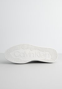 Suela de zapatilla blanca con agarre texturizado, estrías y logotipo embosado de "Calvin Klein". Superficie lisa y duradera con una forma sólida y curvada.
