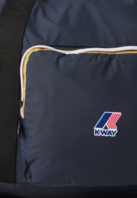 Borsa da viaggio in tessuto blu navy con una tasca con zip contornata in bianco e arancione, con un logo K-WAY blu e rosso ben in evidenza.