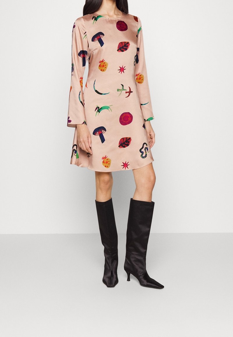 Vaaleanpunainen mekko, jossa on pitkät hihat ja värikäs kuvio sienistä, lehdistä ja muodoista. Yhdistetty polveen asti ulottuviin mustiin satiinikorkkareihin.