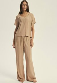Beige loungewear set with a short-sleeve, V-neck top and wide-leg pants, featuring a drawstring waist and smooth, soft texture.
