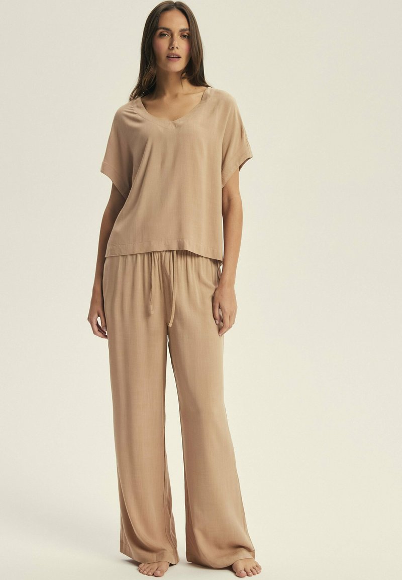 Beige loungewear set with a short-sleeve, V-neck top and wide-leg pants, featuring a drawstring waist and smooth, soft texture.