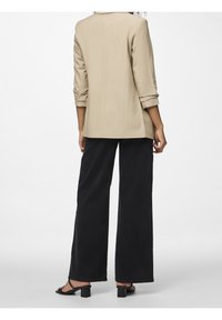 Beige přiléhavý blazer s tříčtvrtečními rukávy, spárovaný s černými širokými kalhotami a černými sandály na blokovém podpatku, zobrazený ze zadní strany.