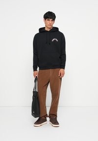 Sort hætte sweatshirt med frontlomme, prydet med hvid og pink tekst. Brune kordfløjspants og mørke sneakers. Sort tote taske inkluderet.