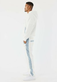 Witte hoodie met blauwe denim accenten, gecombineerd met bijpassende joggers met een blauwe denim streep. Witte sneakers maken de outfit compleet.