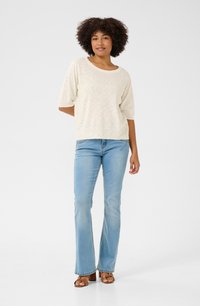 Top en maille beige clair à manches courtes, associé à un jean évasé bleu clair et des sandales à talons marron. Texture lisse, design décontracté.
