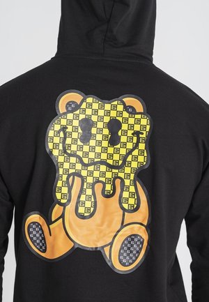 Felpa nera con cappuccio caratterizzata da una grande grafica di un orso cartone con un motivo giallo e nero, design che gocciola e accenti arancioni.