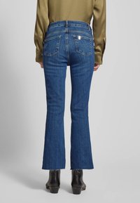 Jeans a zampa d'elefante blu con vita media, caratterizzati da due tasche posteriori e orli sfilacciati. Realizzati in denim con una texture liscia.