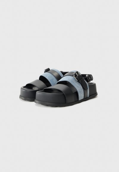 Svart och blå tvåremmade sandaler med en texturerad denimöverdel, släta läderdetaljer, en kraftig sula och ett justerbart spänne.