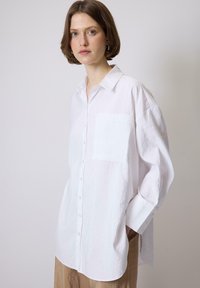 Camicia bianca a maniche lunghe con vestibilità rilassata, dotata di tasca a toppa e texture morbida. Design leggermente oversize con colletto.