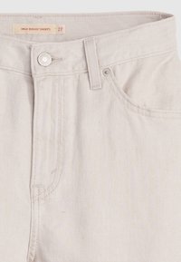 Short beige taille haute ample avec bouton métallique, passants pour ceinture, poche avant et étiquette inscrite « HIGH BAGGY SHORTS 27 » à l’intérieur de la ceinture.