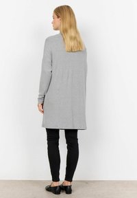 Cardigan lung, gri deschis, cu mâneci lungi și o croială lejeră. Asortat cu blugi skinny negri și pantofi negri fără toc, văzut din spate.