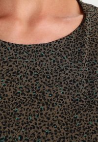 Tissu marron avec un motif léopard noir, agrémenté d'accents turquoise. Encolure ronde et texture lisse.