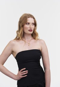 Musta olkaimeton toppi, jossa on istuva muotoilu, sileä pinta ja hienovaraiset sauma-animoinnit. Yhdistetty kullanväriseen kaulakoruun, jossa on pyöreä riipus.