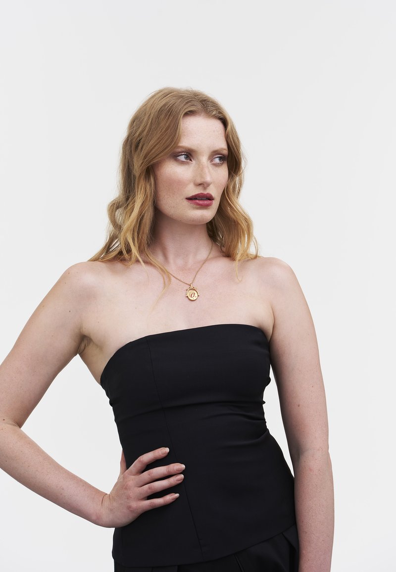 Musta olkaimeton toppi, jossa on istuva muotoilu, sileä pinta ja hienovaraiset sauma-animoinnit. Yhdistetty kullanväriseen kaulakoruun, jossa on pyöreä riipus.