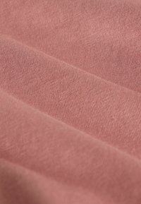 Mäkká, štruktúrovaná tkanina v tlmenej ružovej farbe, ktorá zobrazuje jemné tkané vzory a hladký, mierne elastický povrch.