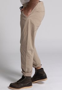 Beige broek van lichtgewicht stof met een elastische tailleband, zijzakken en omslagmanchetten, gecombineerd met donkerbruine veterschoenen.