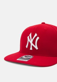 Red snapback cap made of fabric, featuring a white embroidered "NY" logo on the front and a logo tag on the brim.