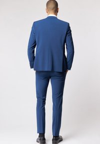 Abito blu con un motivo testurizzato, design aderente e pantaloni slim-fit. La giacca ha una sola fessura e l'insieme è abbinato a scarpe nere.