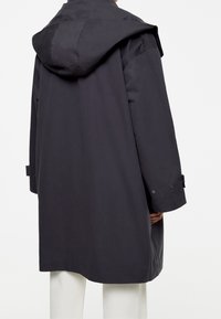 Manteau à capuche gris foncé à coupe décontractée, avec des manches longues et des poignets boutonnés, fabriqué en tissu lisse à finition mate.