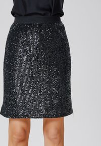 Jupe noire en sequins avec une taille ajustée, texture scintillante et coupe à mi-genoux, conçue avec des lignes verticales de sequins.