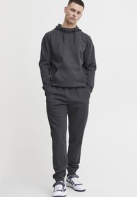 Grey hoodie with adjustable drawstrings, front pocket, and matching sweatpants. Textured fabric, relaxed fit, paired with white and navy sneakers.