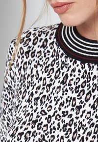 Primer plano de una mujer que lleva un suéter de estampado de leopardo blanco y negro con un cuello a rayas en blanco y negro.
