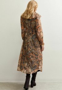 Lang, gestreept jurk gemaakt van lichtgewicht stof met een bruin en zwart paisleypatroon, cinched in de taille met een strik en gathered mouwen.