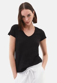 Maglietta nera a scollo a V realizzata in tessuto morbido, maniche corte, vestibilità rilassata, abbinata a pantaloni bianchi con coulisse.
