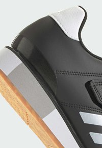 Black athletic shoe with a sleek design, featuring a white leather heel and gray accents. Textured rubber sole for grip and stability.